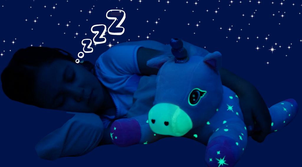 A girl is asleep and hugs Glimmer the Glowing Unicorn who is glowing in the dark